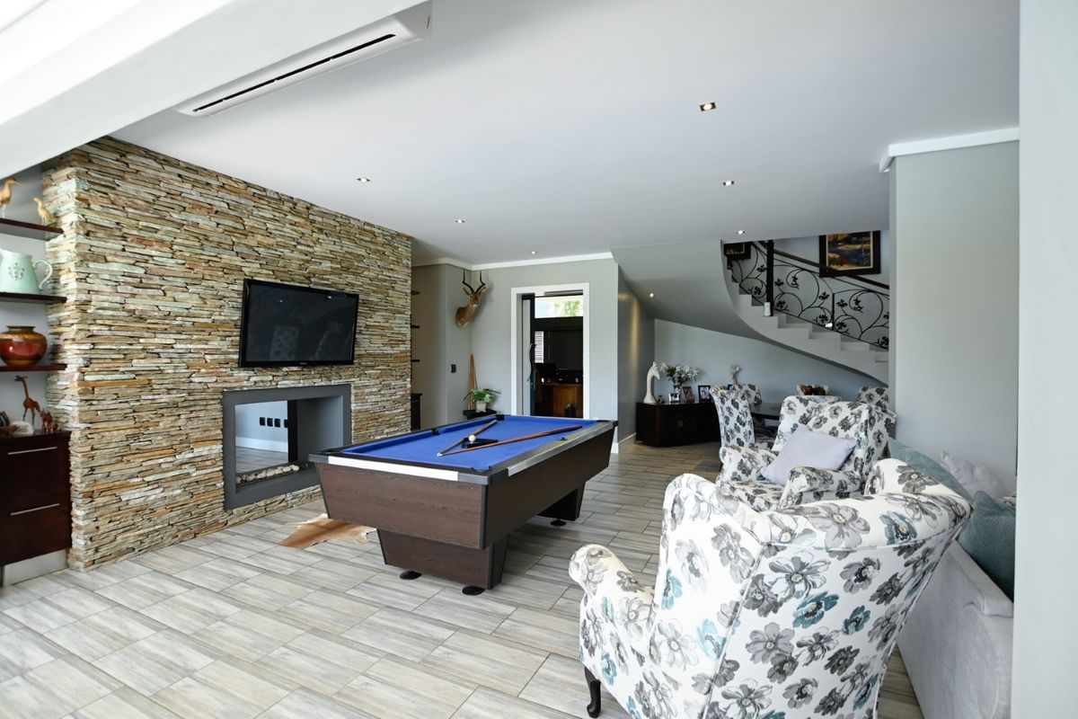 Spacious living area featuring a striking stone feature wall with a built-in fireplace, tiled flooring, and an elegant staircase with wrought iron detailing.