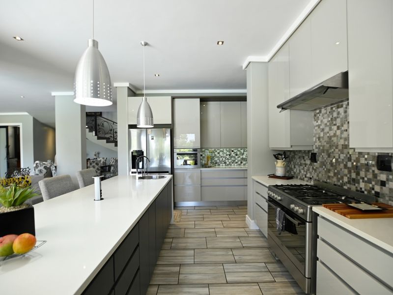 Modern kitchen featuring a large island with quartz countertops, high-end gas range, mosaic backsplash, and sleek cabinetry, seamlessly flowing into the living area.