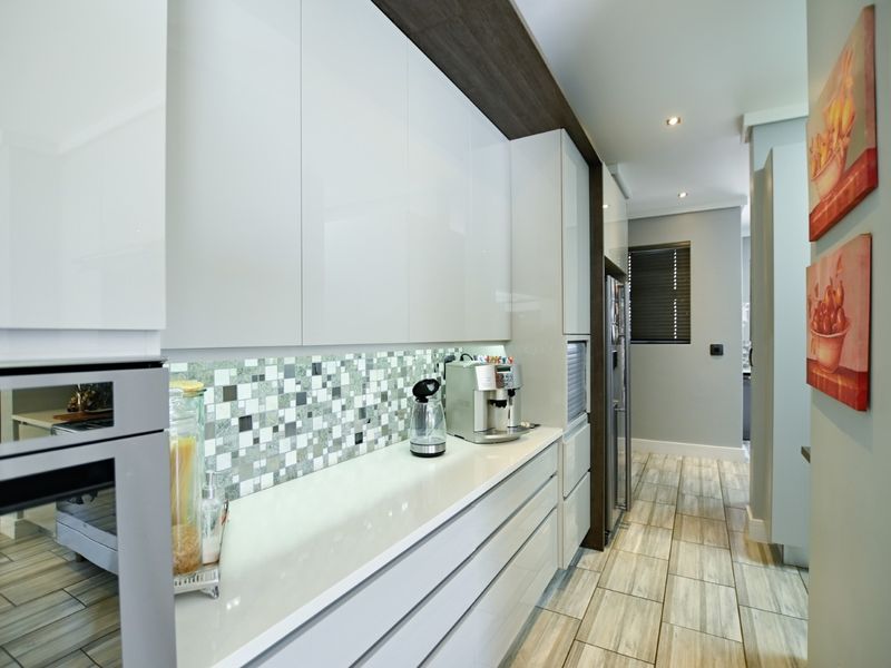 Modern kitchen featuring sleek white cabinetry, a mosaic tile backsplash, stone countertops, and high-quality built-in appliances with contemporary tiled flooring.