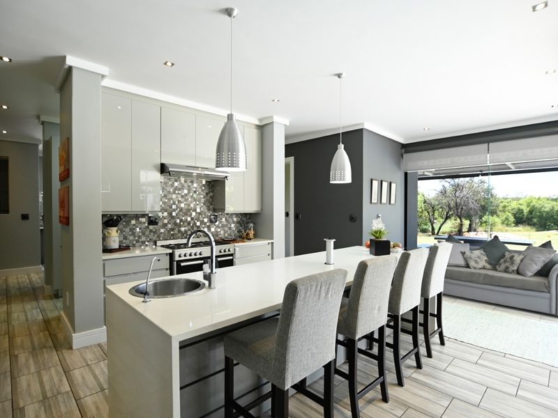 Modern open-plan kitchen featuring a large island with sink, high-gloss cabinetry, mosaic backsplash, and seamless flow to the living area and outdoor patio.