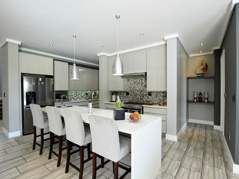 Modern kitchen featuring high-gloss cabinetry, a central island with stone countertops, mosaic tile backsplash, and integrated appliances with contemporary lighting.