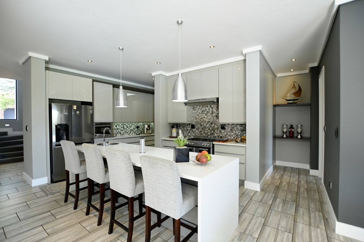 Modern kitchen featuring high-gloss cabinetry, a central island with stone countertops, mosaic tile backsplash, and integrated appliances with contemporary lighting.