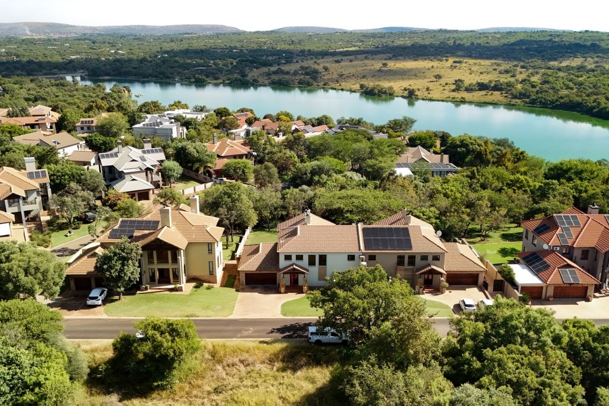 Aerial view of a residential estate featuring homes with tiled roofs, solar panels, and paved driveways, overlooking a scenic lake and natural landscape.