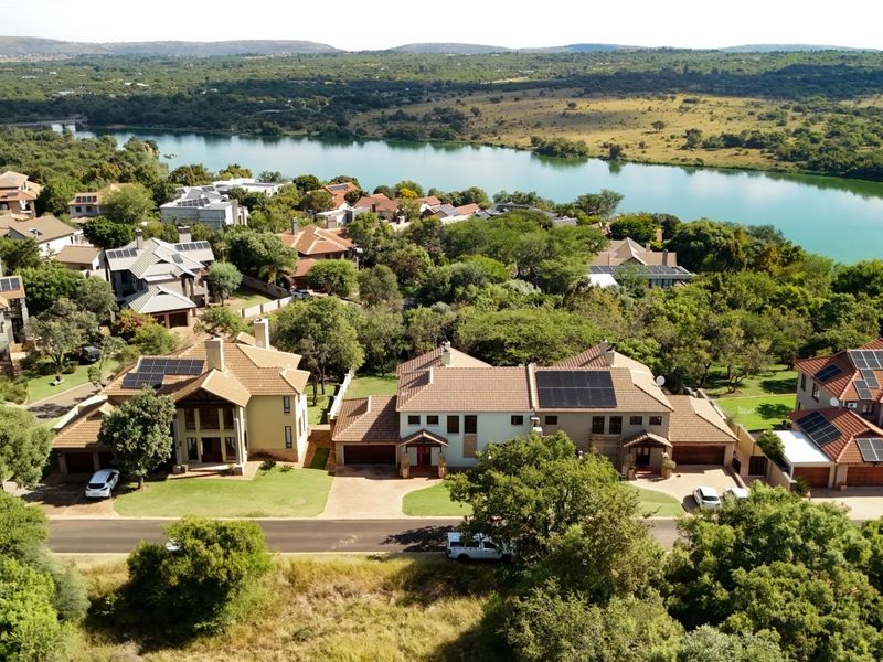 Aerial view of a residential estate featuring homes with tiled roofs, solar panels, and paved driveways, overlooking a scenic lake and natural landscape.