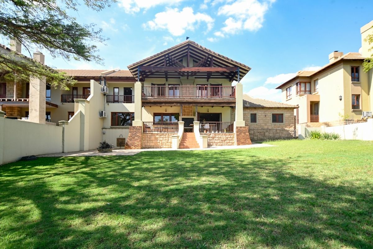 Rear view of a multi-story house featuring a large lawn, timber balcony, stone accents, and exposed roof trusses.