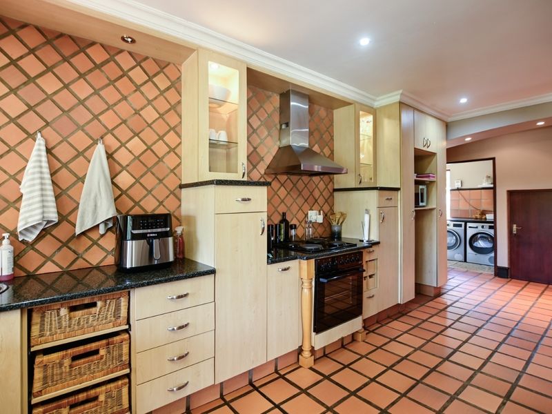 A functional kitchen featuring light wood cabinetry, granite countertops, a built-in oven with gas hob, and a tiled backsplash, with an adjacent laundry area.