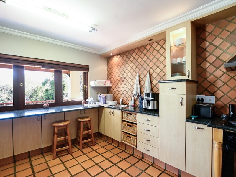 A functional kitchen featuring light wood cabinetry, granite countertops, a built-in oven with extractor fan, and distinctive terracotta floor and wall tiling.