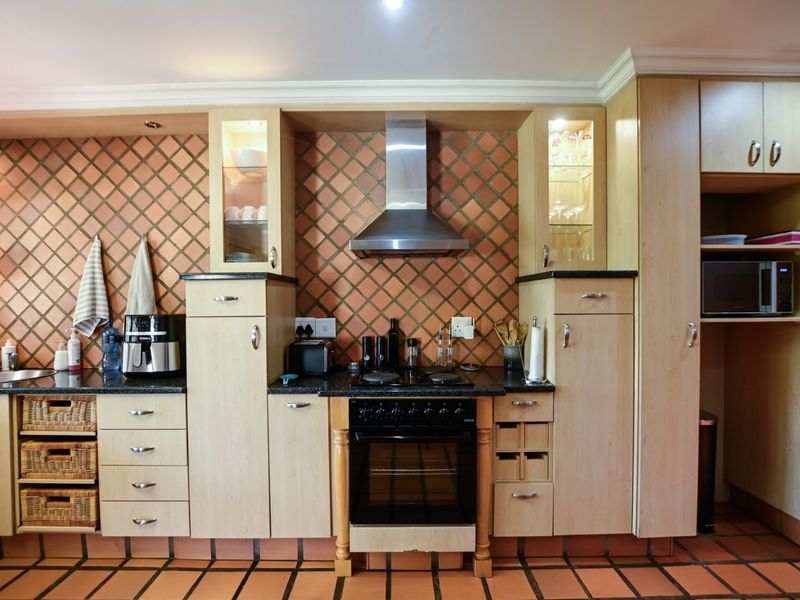 A functional kitchen featuring light wood cabinetry, granite countertops, a built-in oven with extractor fan, and a distinctive tiled backsplash and floor.