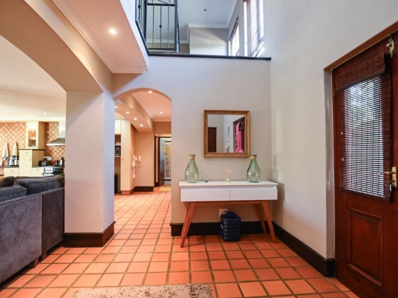 Spacious entrance hall featuring terracotta tile flooring, a double-height ceiling with a wrought iron mezzanine balustrade, and an arched transition to the living area.