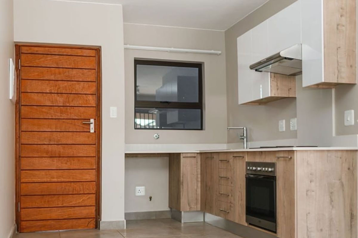 Modern kitchen featuring light wood-grain cabinetry, white upper cupboards, built-in oven, extractor fan, and tiled flooring with a solid timber door.