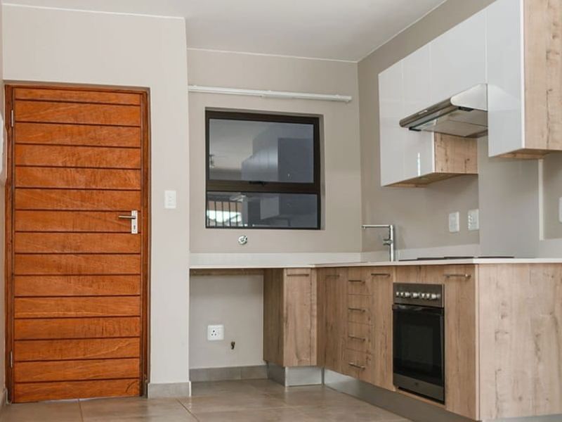 Modern kitchen featuring light wood-grain cabinetry, white upper cupboards, built-in oven, extractor fan, and tiled flooring with a solid timber door.