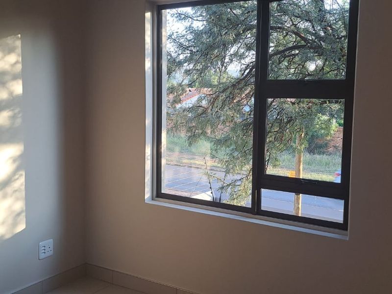 A bright, empty bedroom featuring tiled flooring, a built-in cupboard, and a large aluminium-framed window with a view of the street.
