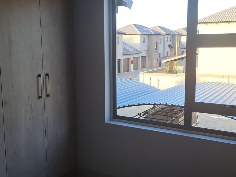 A bright, empty bedroom featuring modern built-in cupboards and a large window overlooking the townhouse complex.