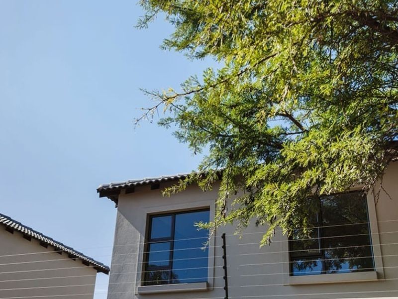 A view of the townhouse exterior featuring tiled roofing, modern aluminium window frames, and installed electric security fencing.