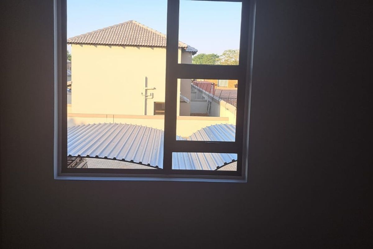 A vacant bedroom featuring built-in cupboards and a large window with views of the surrounding townhouse complex.