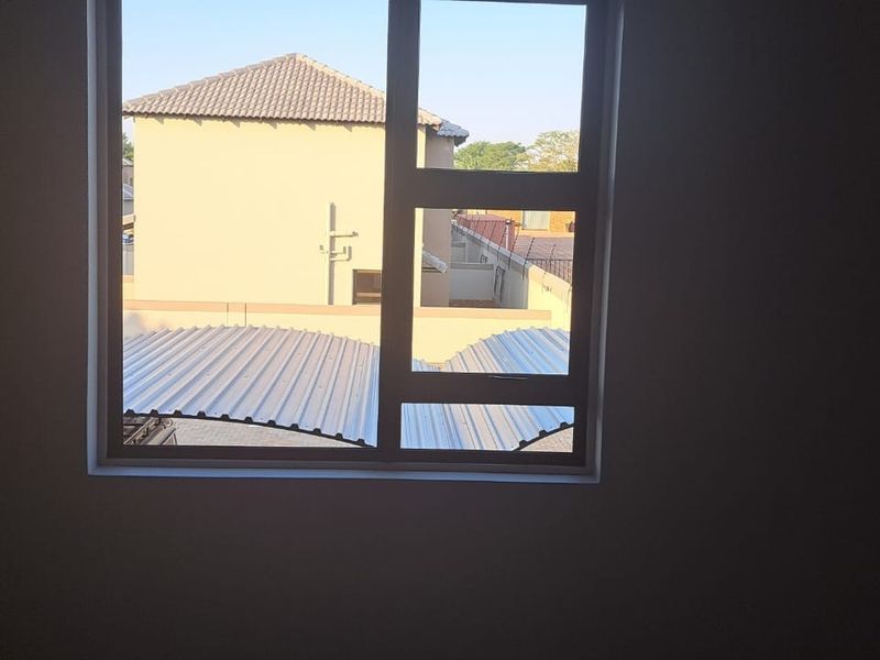 A vacant bedroom featuring built-in cupboards and a large window with views of the surrounding townhouse complex.
