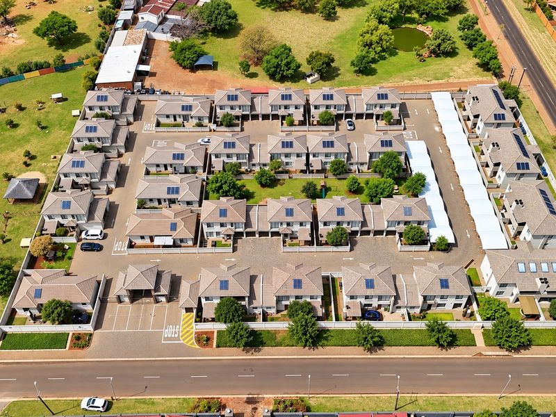 Aerial view of a residential townhouse complex featuring multiple units with solar panels, paved driveways, covered parking, and well-maintained communal garden areas.