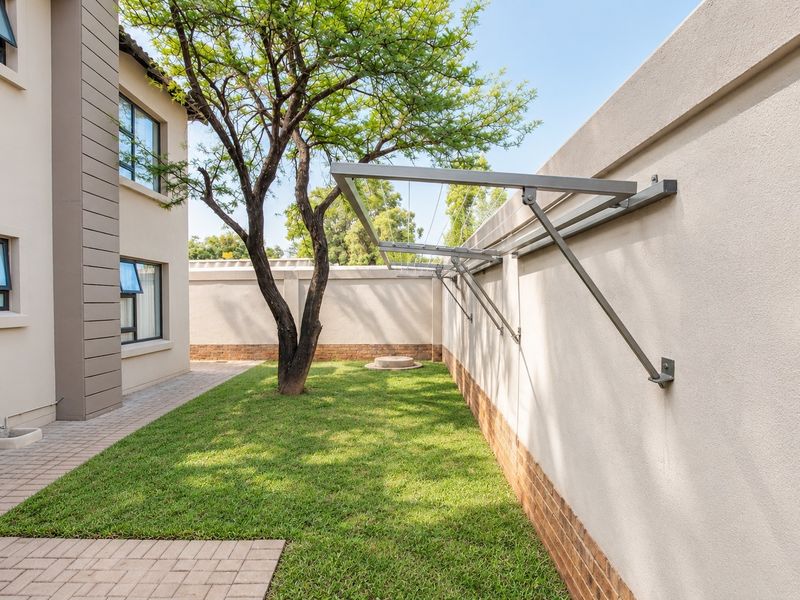A well-maintained rear garden area featuring a paved walkway, manicured lawn, and a practical wall-mounted clothesline attached to the boundary wall.