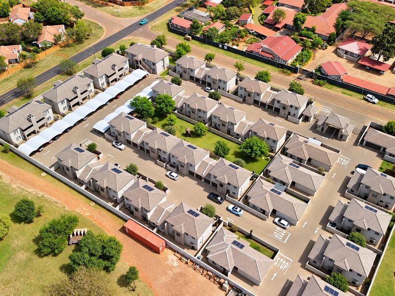 Aerial view of a residential townhouse complex featuring multiple units with tiled roofs, paved driveways, carports, and solar panel installations.