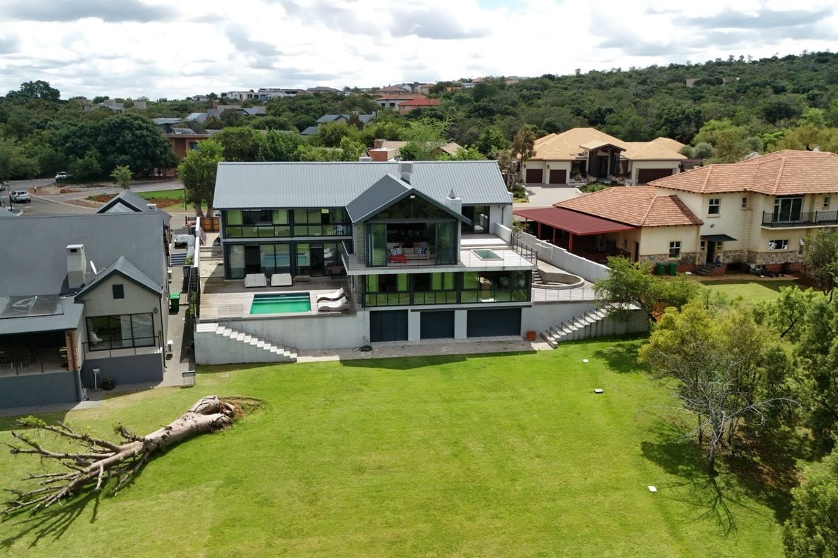 Aerial view of a modern multi-level residence featuring a swimming pool, timber decking, and expansive garden space in a residential estate setting.