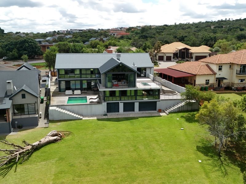 Aerial view of a modern multi-level residence featuring a swimming pool, timber decking, and expansive garden space in a residential estate setting.