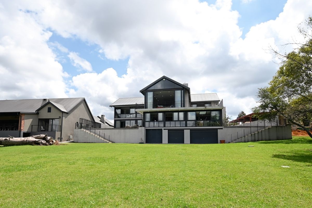 Rear view of a modern multi-level house featuring large glass windows, balconies, and a spacious lawn area.