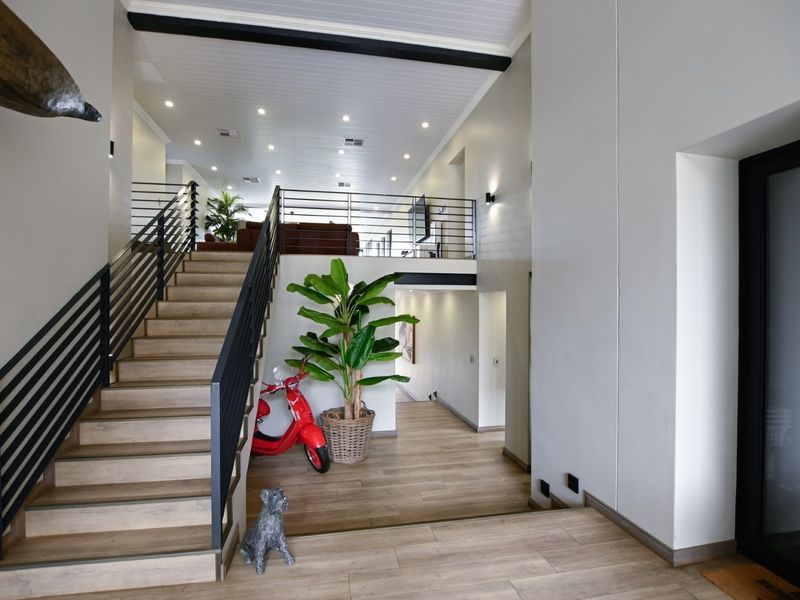 Spacious modern entrance hall featuring a timber staircase with metal balustrades, recessed lighting, and high-quality timber-look flooring leading to an open-plan upper level.