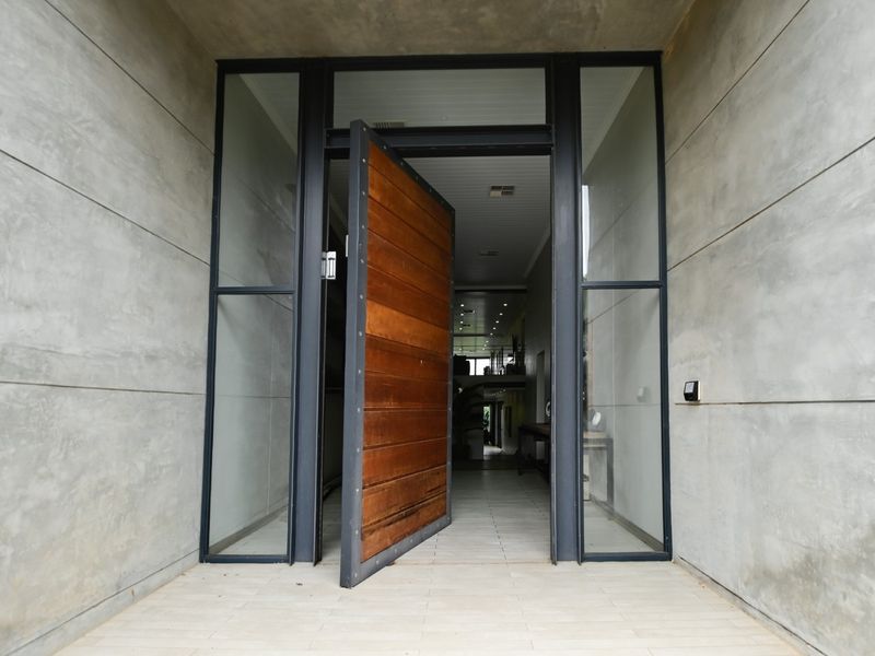 Modern entrance featuring a large timber pivot door, steel framing, and concrete wall panels, leading into a spacious interior hallway.