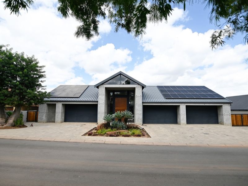 Modern architectural home featuring a concrete facade, triple garage, metal roof with integrated solar panels, and a paved driveway.