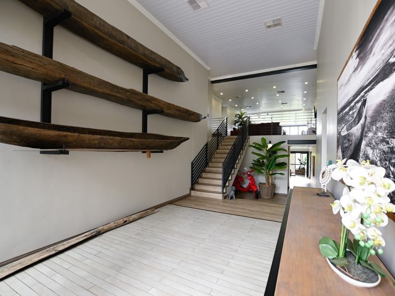 Spacious modern entrance hall featuring a timber staircase with metal balustrade, high ceilings with recessed lighting, and tiled flooring.