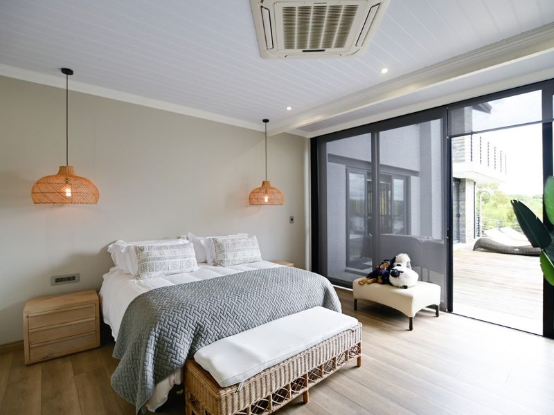 A modern, well-maintained bedroom featuring timber flooring, a tongue and groove ceiling, integrated air conditioning, and large sliding glass doors leading to a deck.