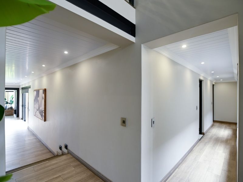 A bright and modern hallway featuring clean white walls, recessed downlighting, tongue and groove ceiling panels, and light-toned laminate flooring.