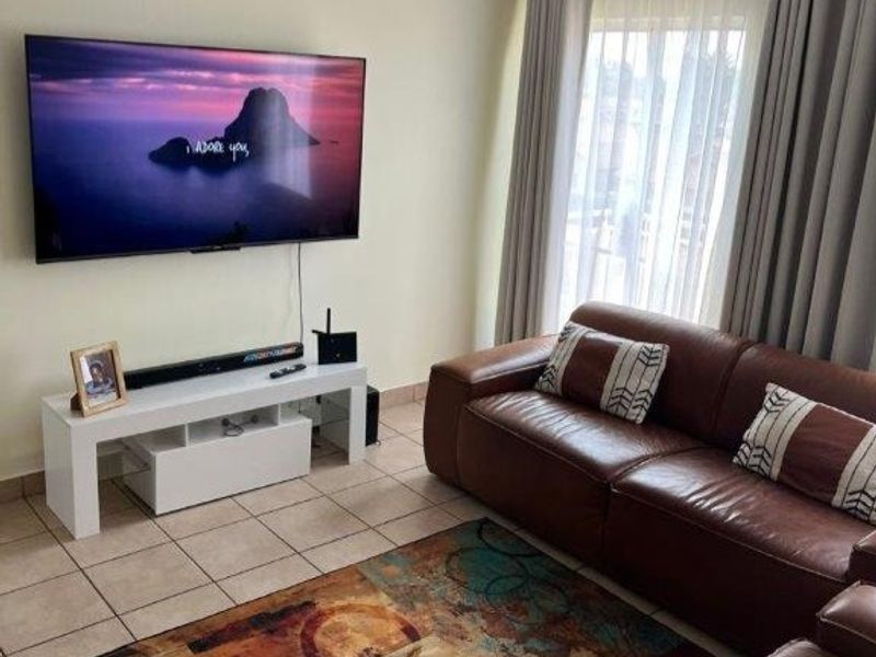 A comfortable living room featuring tiled flooring and a large sliding door with curtains, providing natural light and access to the exterior.