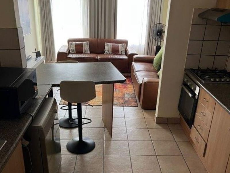 Open-plan living area featuring a functional kitchen with built-in cabinetry, gas hob, and oven, seamlessly flowing into a comfortable lounge space with tiled flooring.
