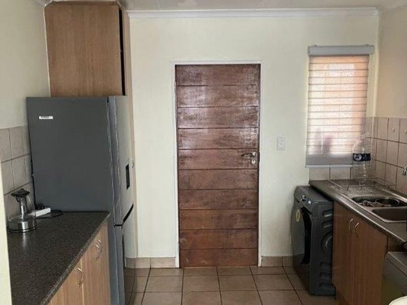 A functional kitchen featuring laminate cabinetry, tiled flooring, and a tiled backsplash, offering a practical layout with potential for modern cosmetic updates.