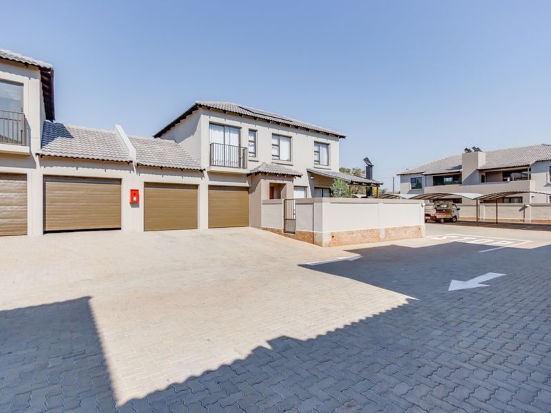 Front view of a modern townhouse complex featuring a triple garage, paved driveway, and upper-level balcony access.
