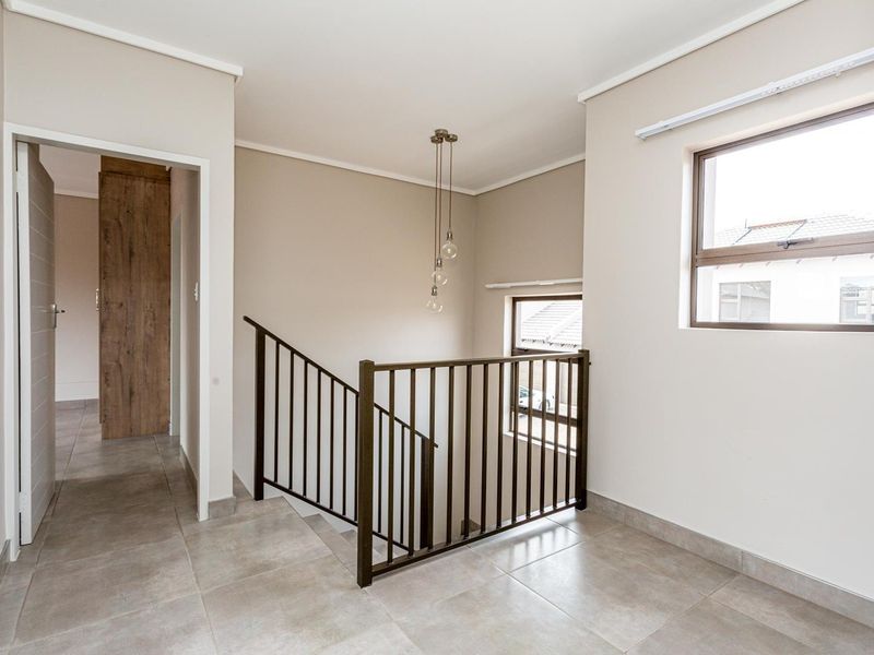A bright and modern landing area featuring tiled flooring, a metal staircase balustrade, and contemporary pendant lighting.