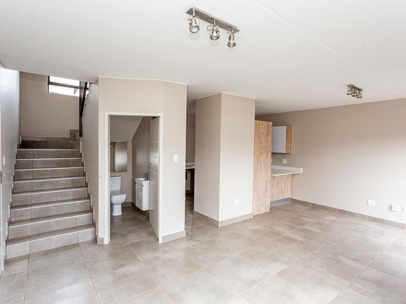 An open-plan living area featuring tiled floors, modern spotlighting, a staircase, and a compact guest bathroom with a vanity and toilet.
