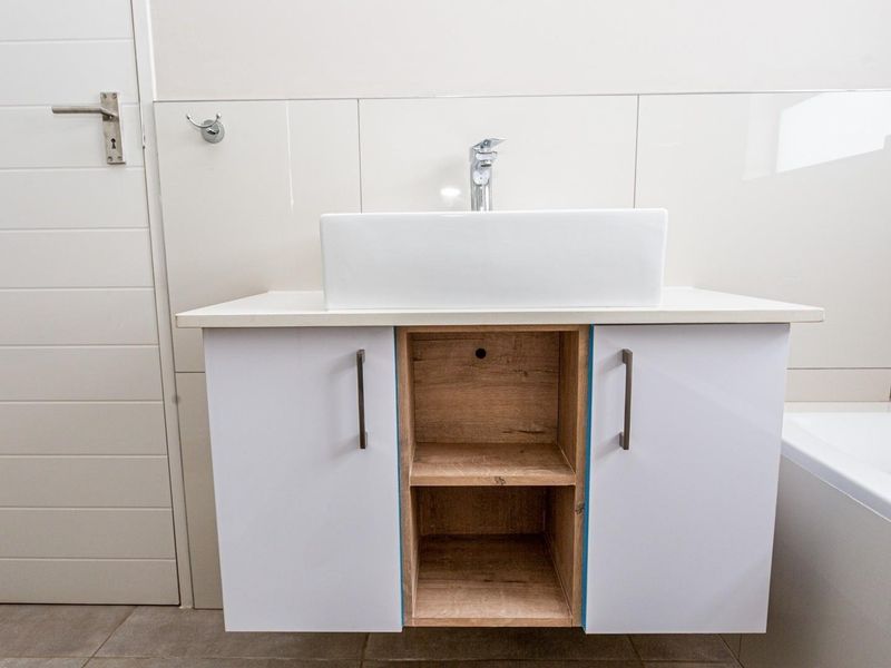 A modern bathroom vanity featuring a white vessel sink, chrome faucet, and a combination of white and wood-grain cabinetry.