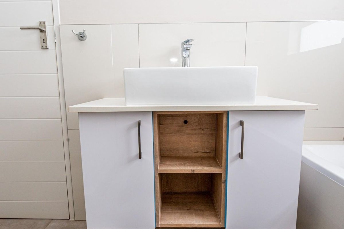 A modern bathroom vanity featuring a white vessel sink, chrome faucet, and a combination of white and wood-grain cabinetry.