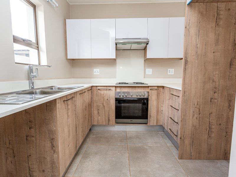 Modern kitchen featuring wood-look cabinetry, stone countertops, built-in oven, electric hob, extractor fan, and a double sink with a mixer tap.