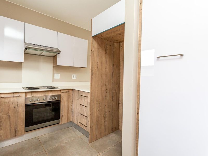 Modern kitchen featuring wood-grain and white cabinetry, built-in oven, electric hob, extractor fan, and neutral tiled flooring.