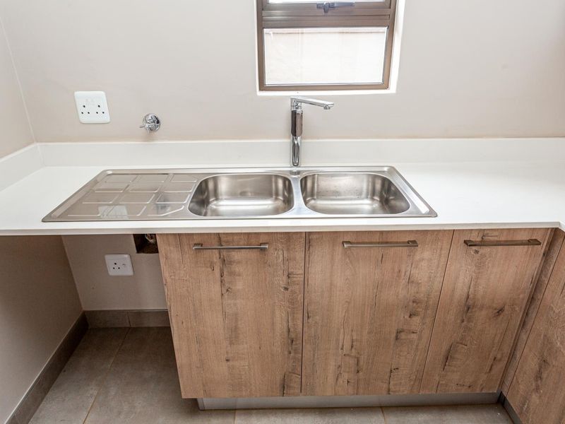 A clean and modern kitchen area featuring a double stainless steel sink, wood-look cabinetry, and stone countertops under a window.
