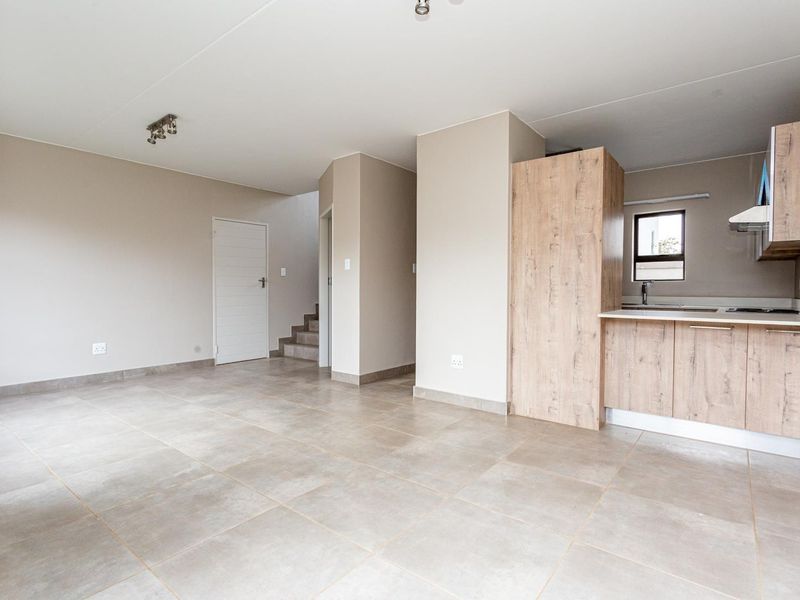 An open-plan living and kitchen area featuring neutral tiled flooring, modern wood-look cabinetry, and a staircase leading to the upper level.