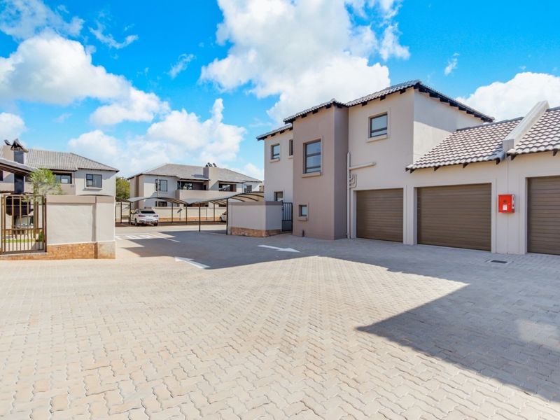 A well-maintained townhouse exterior featuring a paved driveway, double garage, and modern architectural finishes within a secure residential complex.