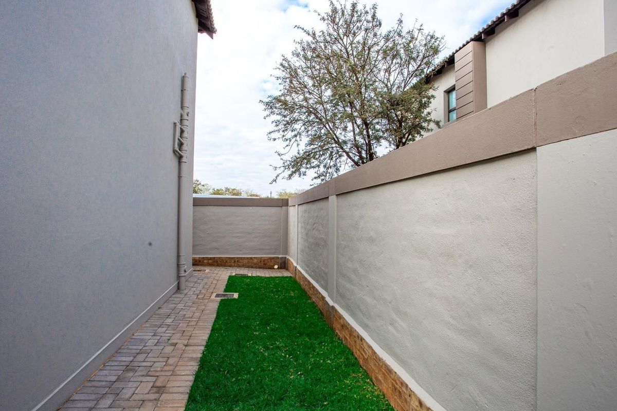 A side garden area featuring a paved walkway, a small patch of lawn, and high boundary walls for privacy.