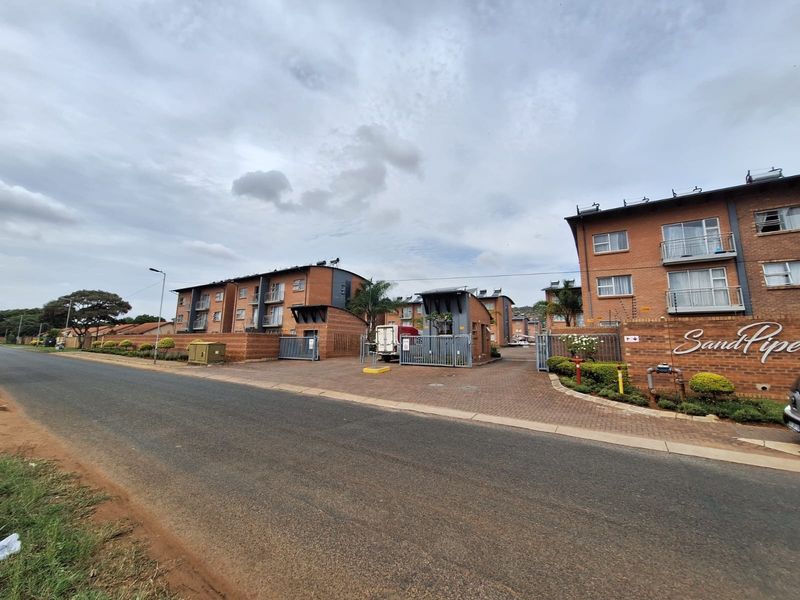 Street view of the Sandpiper apartment complex entrance, featuring brick facade buildings, secure gated access, paved driveway, and balconies.
