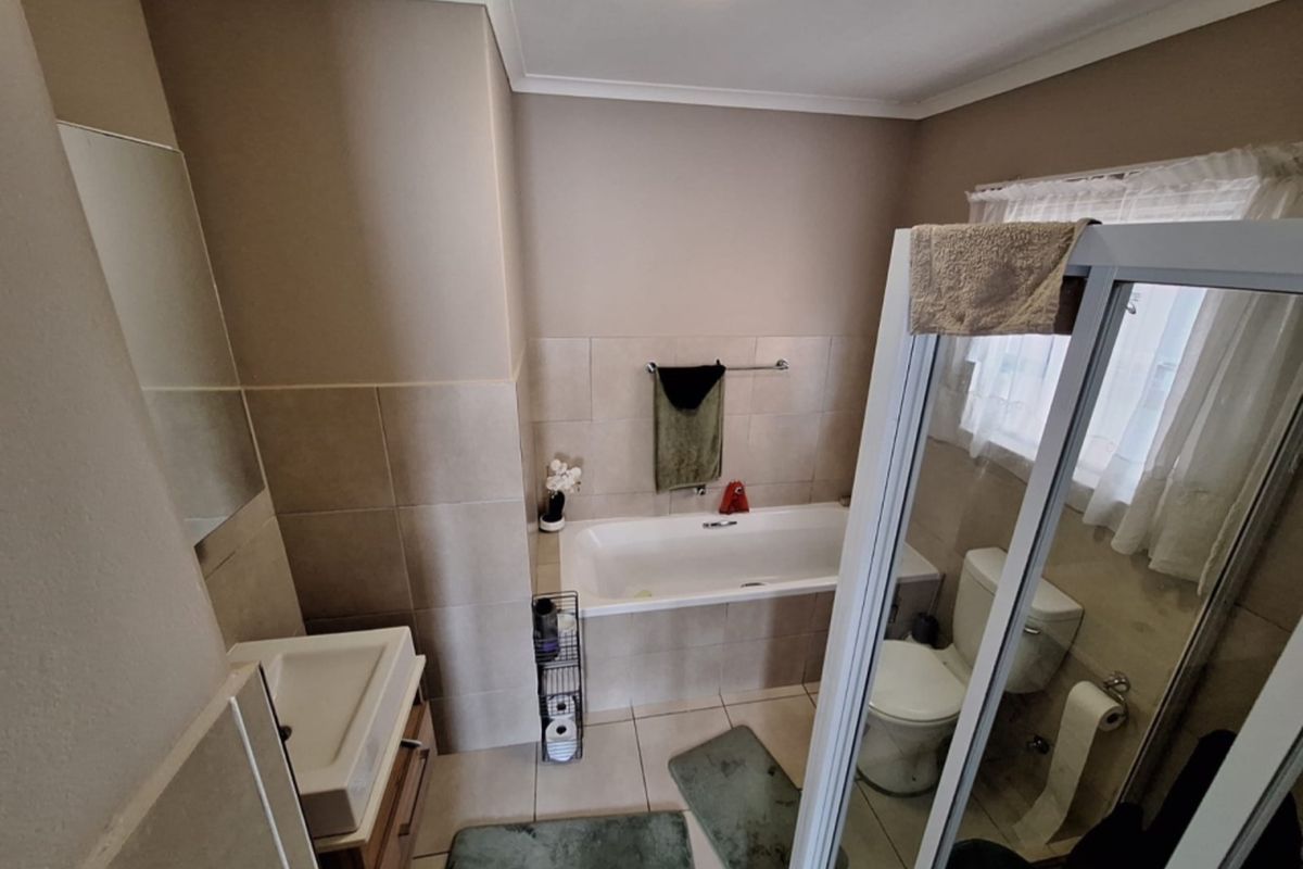 A functional bathroom featuring a built-in bathtub, separate shower enclosure, wall-mounted vanity basin, and neutral ceramic tiling throughout.