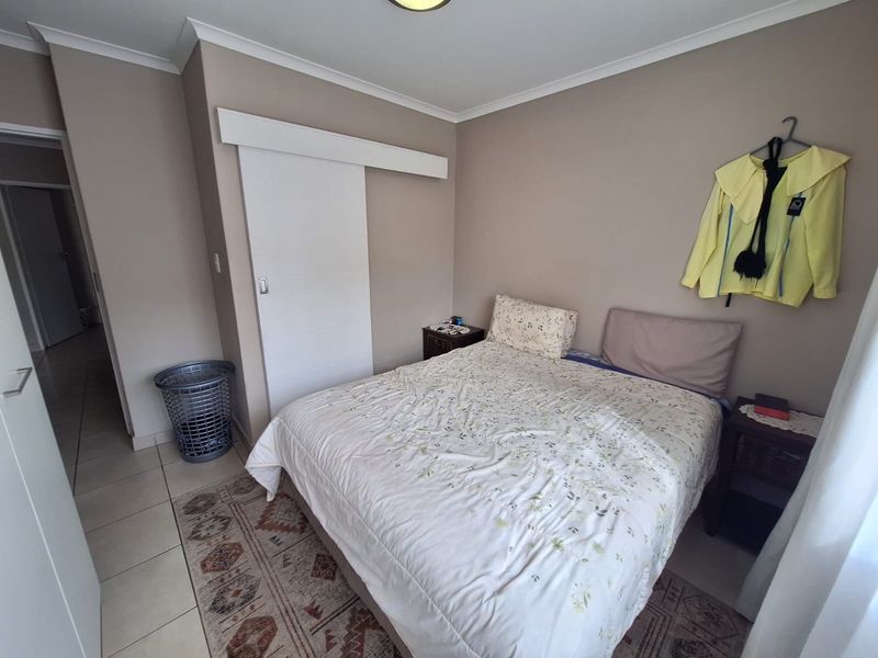 A functional bedroom featuring tiled flooring, a sliding door, and neutral wall tones, offering a clean and practical living space.
