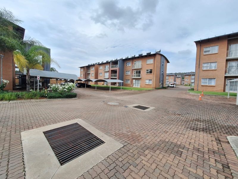 Exterior view of a residential apartment complex featuring brick-paved driveways, covered parking structures, and multi-story brick buildings with balconies.